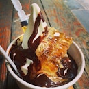 Yogurt drenched in hot chocolate fudge with a syringe of honey and a honeycomb by the side.