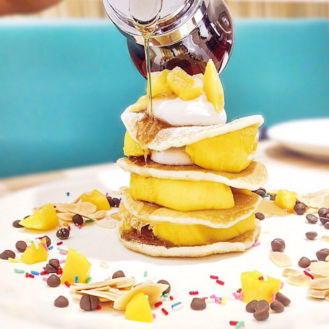 Nicely stacked mini pancakes with mango and whipped cream.